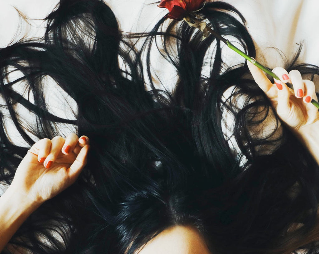 woman's beautiful black hair laying down with rose in hand coconut hair oil amla hair oil for thick hair growth